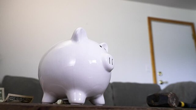 Slow motion footage of a white piggy bank and sledgehammer with dollar bills flying around