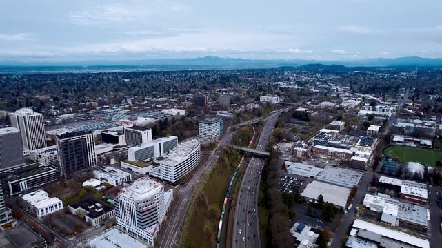 Wide aerial panoramic view of a modern urban landscape featuring a major highway with traffic flow, commercial office buildings, and residential districts under a clear sky during daytime
