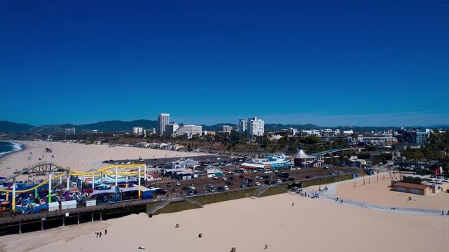 High-angle aerial view of the iconic Santa Monica beach and parking lots under a clear blue sky, showcasing the coastal city skyline and sandy shoreline in California, United States