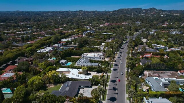 Aerial view of Beverly Hills residential neighborhood with luxury mansions, swimming pools, and palm trees under a clear blue sky in Los Angeles, California, showcasing wealthy suburban living