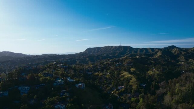 Panoramic aerial view of the lush Hollywood Hills in Los Angeles, California, showcasing the sprawling residential landscape and mountainous terrain under a clear blue sky during a bright day