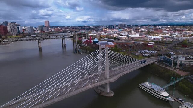 Aerial perspective of the Tilikum Crossing cable-stayed bridge spanning the Willamette River in Portland, Oregon, showcasing the urban cityscape, river traffic, and infrastructure under overcast skies
