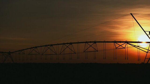 Silhouette of a center pivot irrigation system stretching across a vast agricultural field during a vibrant golden sunset, highlighting modern farming technology and water management