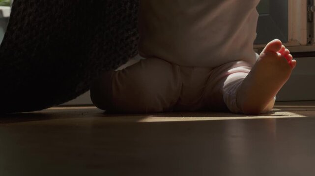 Baby sitting on wooden floor plying with carpet on a sunny day.