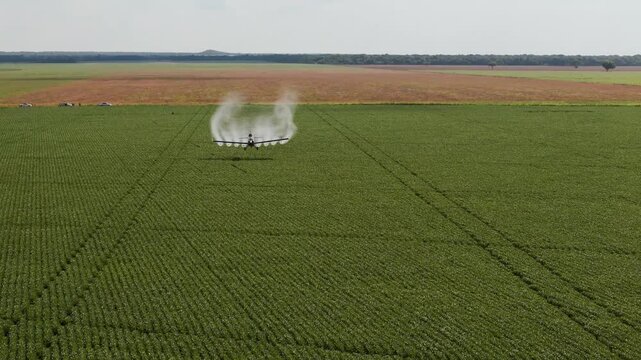 Aerial shot of a crop duster airplane flying low over a vast green agricultural field, spraying pesticides or liquid fertilizer to protect crops and ensure a healthy harvest in the countryside