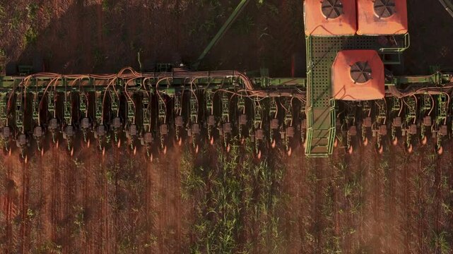 Aerial top-down view of a modern industrial agricultural planter machine sowing seeds in a vast farm field during the planting season, showcasing advanced technology in large-scale farming