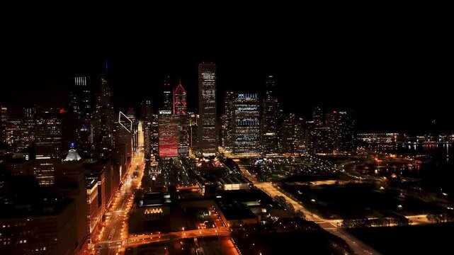 Panoramic night view of the Chicago city skyline featuring illuminated skyscrapers, glowing urban streets with traffic, and iconic architectural landmarks under a dark sky in the United States