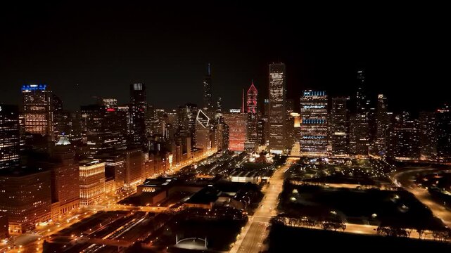 Stunning aerial panorama of the Chicago city skyline at night featuring illuminated skyscrapers and glowing city streets with traffic light trails under a dark sky in the United States