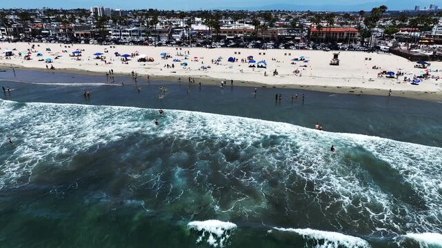 A Drone UAV Aerial view of he Newport Beach Pier Commerce area in California looking at the wave and the ocean in the surf  zone and people swimming, and Picnicking on the Beach