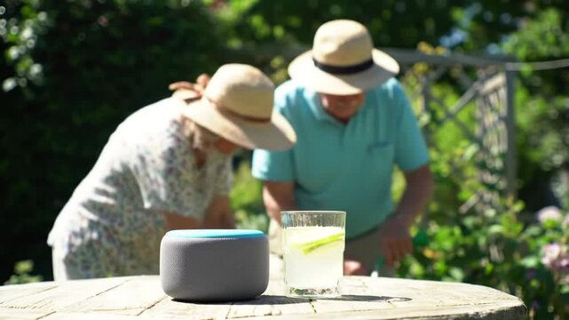Elderly couple enjoying garden, smart speaker and drink on table