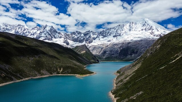 Drone aerial view of Pemahling Lake surrounded by rugged valleys and the snow-covered Kula Khangri massif in the Tibetan Himalayas, Lhoka, Tibet.