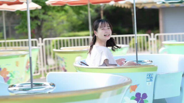 遊園地のコーヒーカップに乗って笑顔を見せる若い女性と中年女性（母娘の休日）