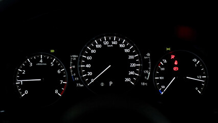 Fototapeta premium Dashboard display of a modern car showing speedometer, tachometer, fuel gauge, and warning lights illuminated against a dark background
