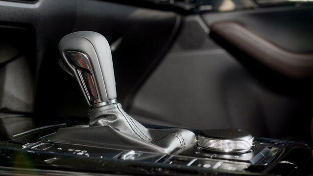 Car interior featuring automatic transmission gear shift lever with leather boot and control knob on center console, showcasing modern automotive design elements