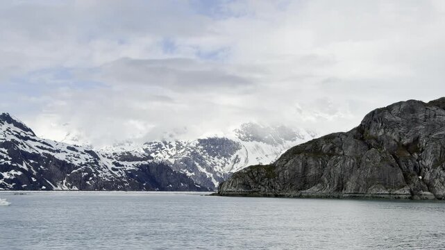 A lonely bergy bit drifts past a dark headland under snowy peaks