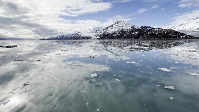 Glassy turquoise water mirrors a bright sky scattered with brash ice