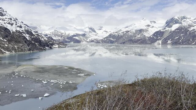 From a tundra bluff a calm ice-flecked bay rests below snowy peaks
