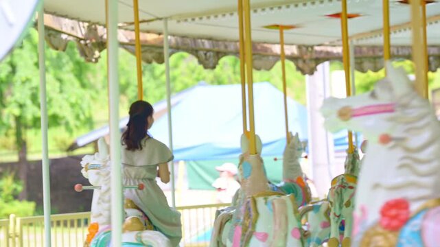 遊園地のメリーゴーランドに乗って笑顔で振り返る若い女性（休日のデート・レジャー）