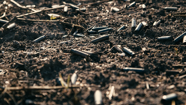 Spent bullet casings scattered across a dirt field with dry grass and soil visible, indicating a shooting range or hunting area in a rural setting