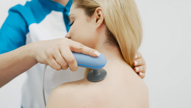 Female clinician using shockwave therapy device on patient&rsquo;s shoulder to treat muscle pain. Concept physiotherapy, healthcare and rehabilitation.
