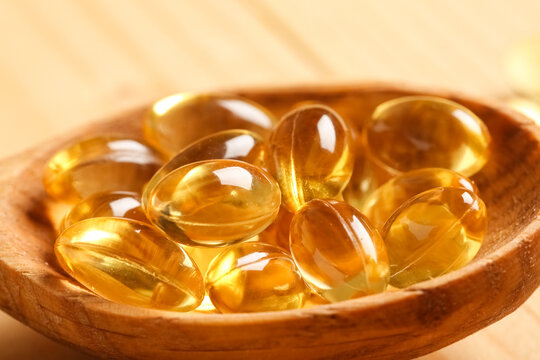 Close-up of yellow soft gel capsules in wooden spoon