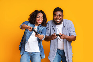 Obraz premium Smiling Black Man And Woman Enjoying Time Together While Playing Video Games, Holding Controllers, In A Fun Atmosphere At The Studio, Engaged In Gaming Activity. Great For Gaming Concept.