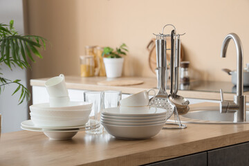 Fototapeta premium Clean white dishes and kitchen utensils on wooden countertop near sink