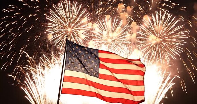 American flag waving with bright fireworks exploding in the night sky.