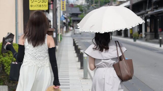 古い城下町の風情ある町並みを日傘を差して観光する職場の上司と部下の女性（後ろ姿）