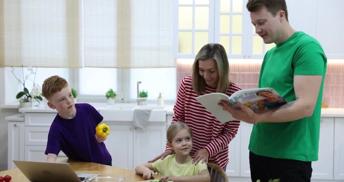 Parents and their kids making salad at wooden table in kitchen, camera moving in