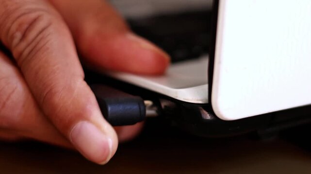 Close up of a hand inserting a DC power jack charger cable into a laptop port, device charging and daily work routine concept.