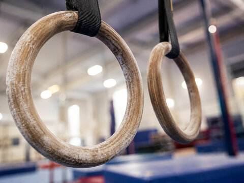 Wooden gymnastic rings hanging in a modern gym, strength training close-up with chalked texture and shallow depth of field