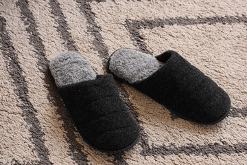Pair of black and gray cozy slippers on patterned carpet © Pixel-Shot
