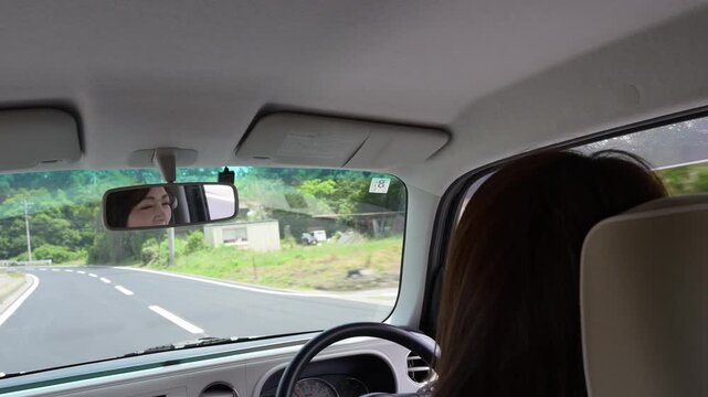 後部座席からの視点 ルームミラーに映る運転する女性と田舎道のドライブ風景
