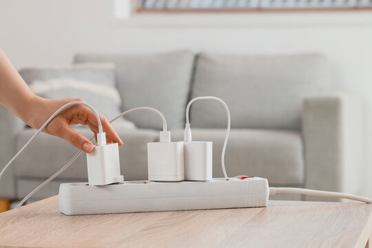 Hand plugging charger into power strip on wooden table in living room