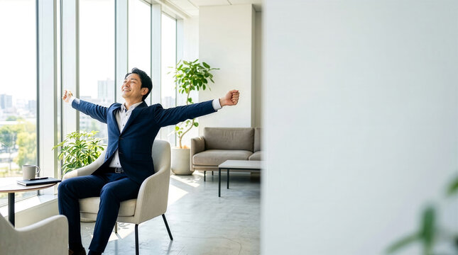明るいオフィスの窓際で椅子に座り大きく伸びをしてリフレッシュするスーツ姿の男性ビジネスマン。休憩や達成感、ウェルビーイングのコンセプト。コピースペースあり