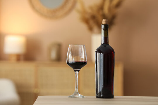 Glass of red wine and corked bottle on table in cozy living room