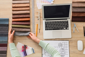 Naklejka premium Female interior designers hands with fabric samples and blank laptop on table, top view