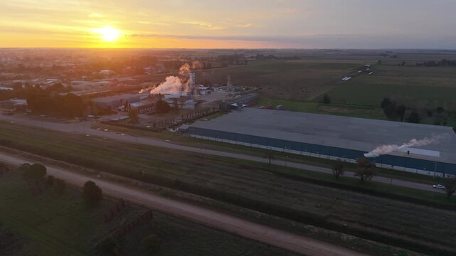 F&aacute;brica industrial con chimeneas emitiendo humo en un pueblo rural al amanecer. Industria, producci&oacute;n, energ&iacute;a, desarrollo econ&oacute;mico, trabajo, infraestructura, paisaje rural