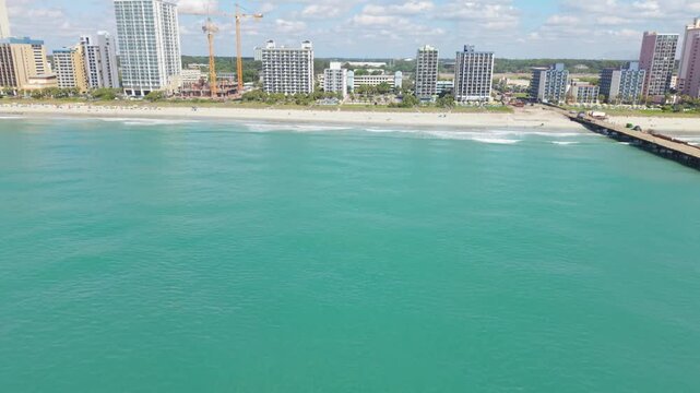 Aerial perspective of Myrtle Beach, South Carolina, highlighting turquoise ocean waves gently rolling onto the sandy beach with coastal structures