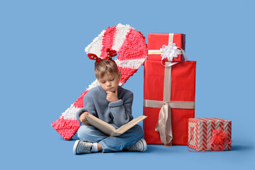 Naklejka premium Thoughtful little boy with Christmas gifts reading book on blue background