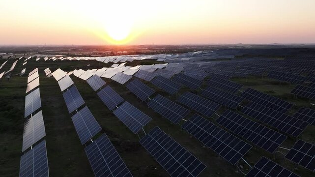 Large photovoltaic power station array landscape during sunset with solar panels aligned on open fields