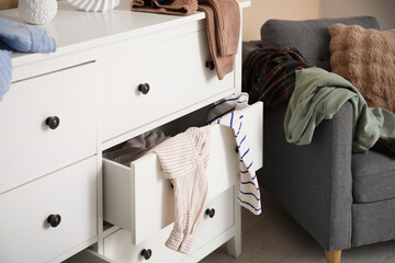Fototapeta premium Stylish commode with different scattered clothes near beige wall in room, closeup