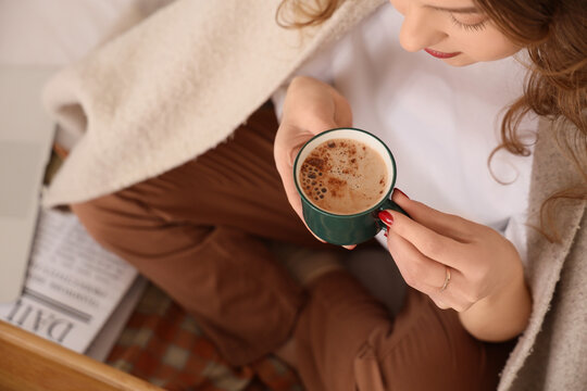 Beautiful young woman with cup of tasty coffee and plaid sitting at home, closeup
