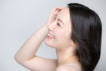 Fototapeta premium 笑顔で風になびく美しい女性 素肌と艶やかな髪が印象的な美容ビューティーポートレート 笑顔でクローズアップ 髪をかき上げる横顔