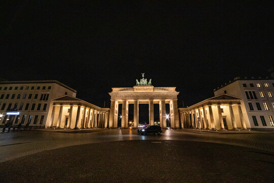 View of the illuminated Brandenburg Gate at night with neoclassical architecture and a car driving through the square in Berlin, Berlin, Germany.