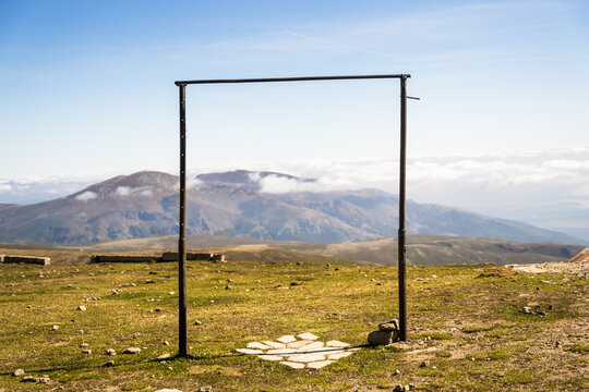 View of Botev Peak framed by a metal structure on a grassy mountain landscape under a clear blue sky in Balkan Mountains, Lovech, Bulgaria.