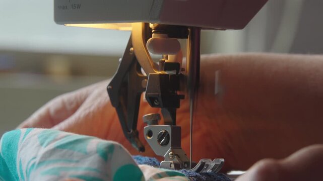 Close up of sewing machine needle stitching as woman feeds frilly blue fabric through, indoor setting