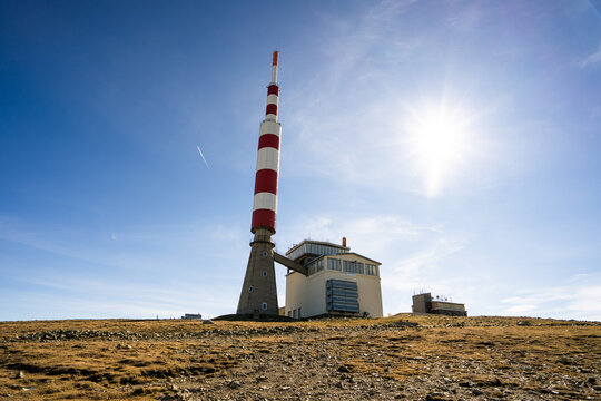 View of Botev Peak with its red and white telecommunications tower and adjacent building under a bright blue sky in the Balkan Mountains, Lovech, Bulgaria.
