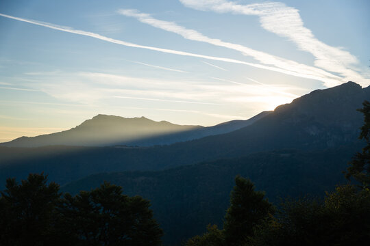 View of Botev Peak at sunrise with soft light rays, silhouetted mountain ridges, and wispy clouds in the sky, Balkan Mountains, Lovech, Bulgaria.